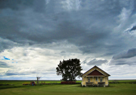Abandoned farmhouse sits on a flat horizon, menacing storm clouds overhead, Saskatchewan - Photo by David Innes